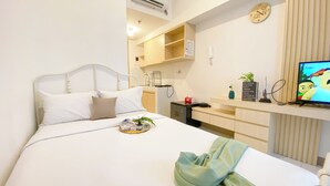 A hotel room with a bed, a small kitchenette, a TV, and a wall clock. - Good And Cozy Studio Apartment At Tokyo Riverside Pik 2 (Teluknaga)