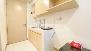 A small kitchenette with a sink, a coffee maker, and a toaster. There is a door to the left and a small table with a box of tissues on the right. - Good And Cozy Studio Apartment At Tokyo Riverside Pik 2 (Teluknaga)