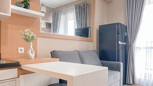A modern hotel room with a desk, a grey sofa, a dark cabinet, and a large window with curtains. - Best Choice And Homey 1Br Apartment Royal Olive Residence (Jakarta)