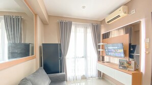 A modern living room with a grey sofa, a flat-screen TV, a wooden entertainment unit, and a large window with curtains. - Best Choice And Homey 1Br Apartment Royal Olive Residence (Jakarta)
