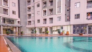 A swimming pool with a tiled deck, surrounded by a multi-story building with balconies and large windows. - Best Choice And Homey 1Br Apartment Royal Olive Residence (Jakarta)
