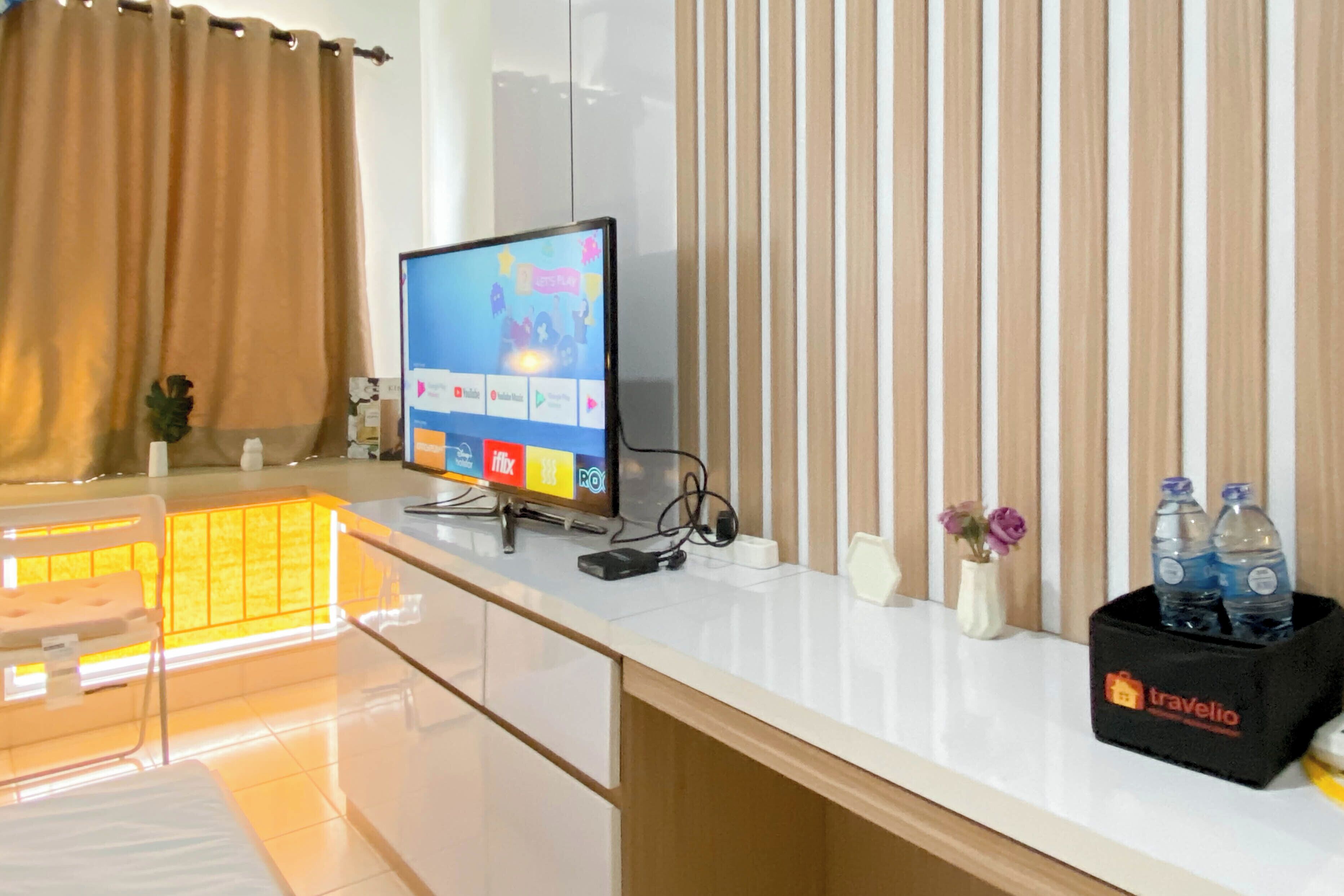 A hotel room with a flat-screen TV, a minibar, a tray table, and a minibar with bottled water.