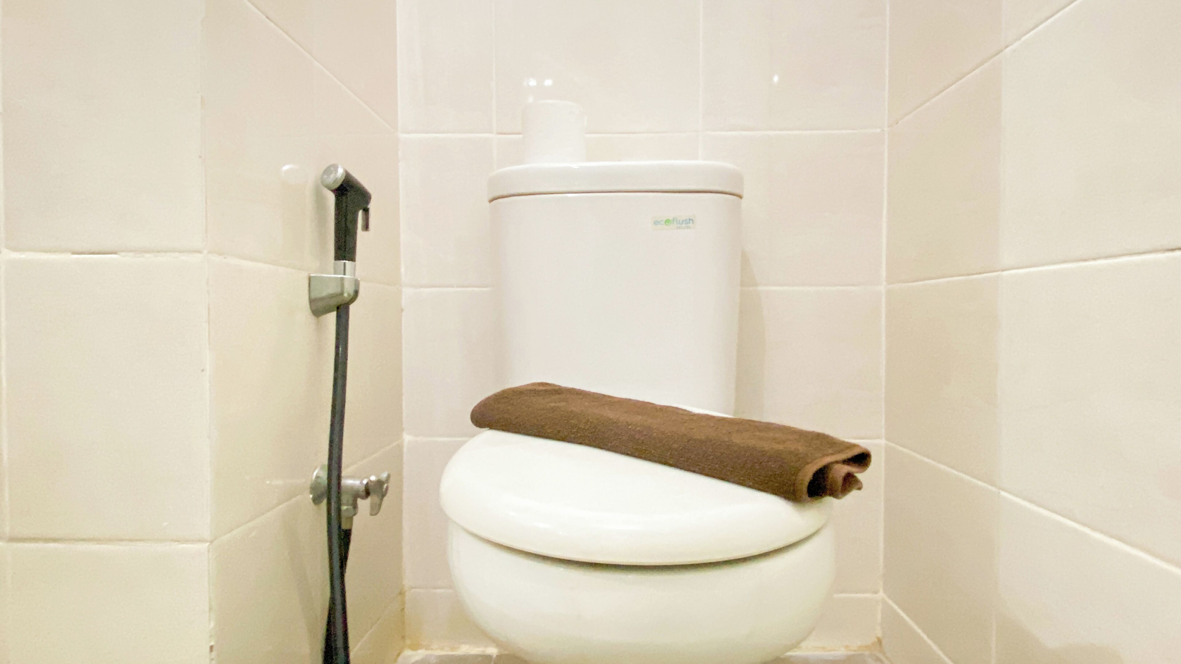 Un inodoro blanco con una toalla marrón encima, un dispensador de papel higiénico y una manguera de ducha.