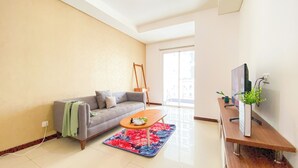 A living room with a grey sofa, a wooden coffee table, and a TV on a wooden stand. - Homey And Comfort 2Br Green Bay Condominium Apartment (Jakarta)