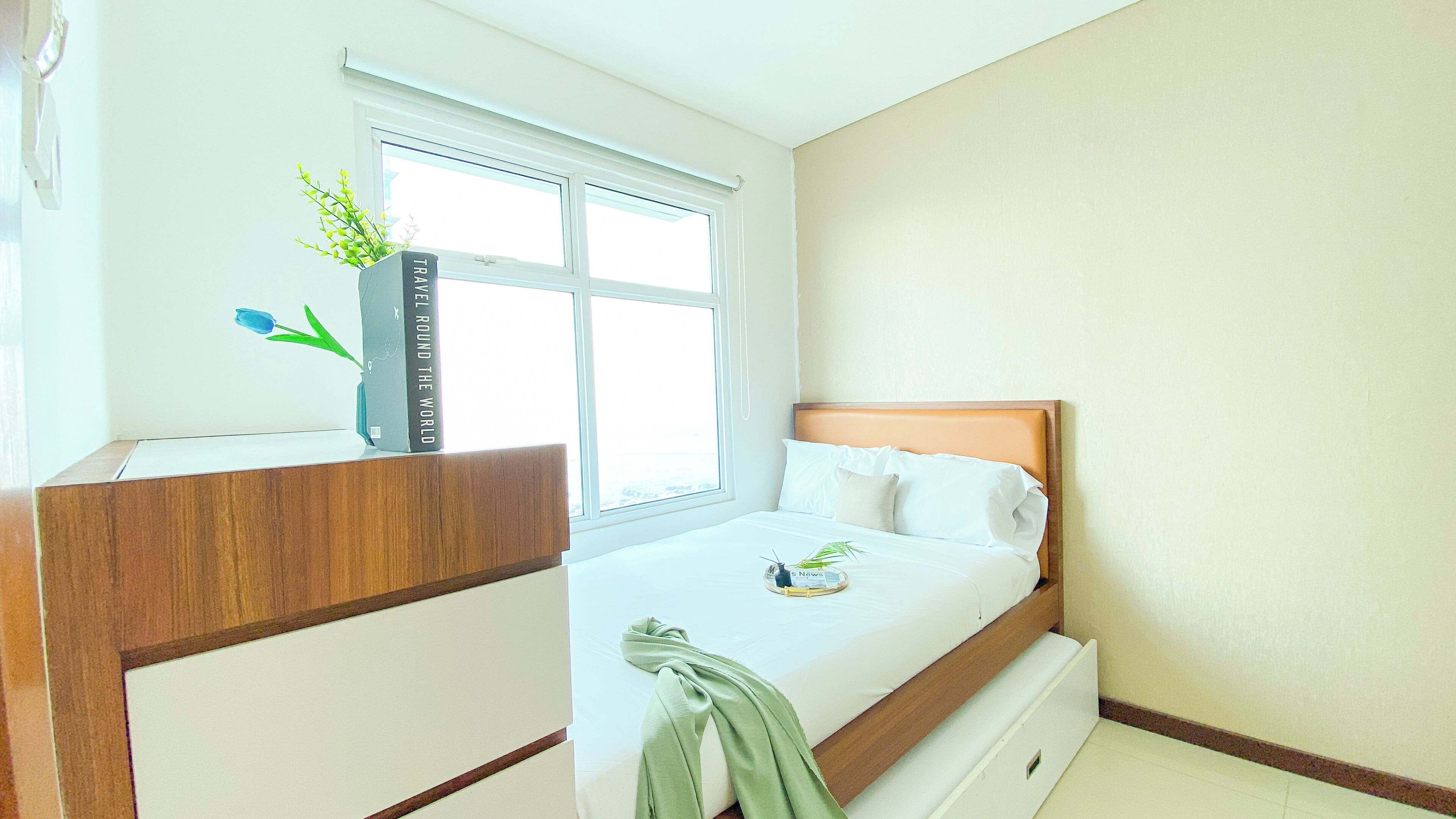 A neatly arranged bedroom with a bed, a bedside table, a window, and a small plant.