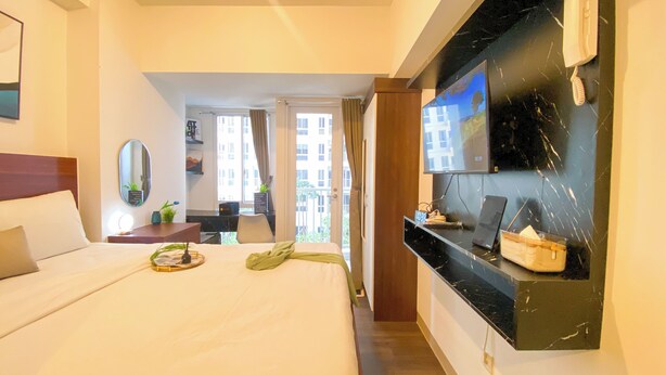 Ein Hotelzimmer mit einem großen Bett, einem Wand-Fernseher, einem kleinen Schreibtisch mit Lampe und Blick auf den Balkon.