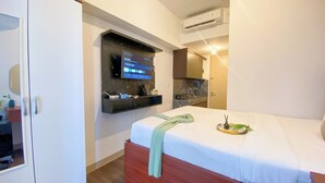 Ein Hotelzimmer mit Bett, Wandfernseher, einer kleinen Küchenzeile und einer Klimaanlage.