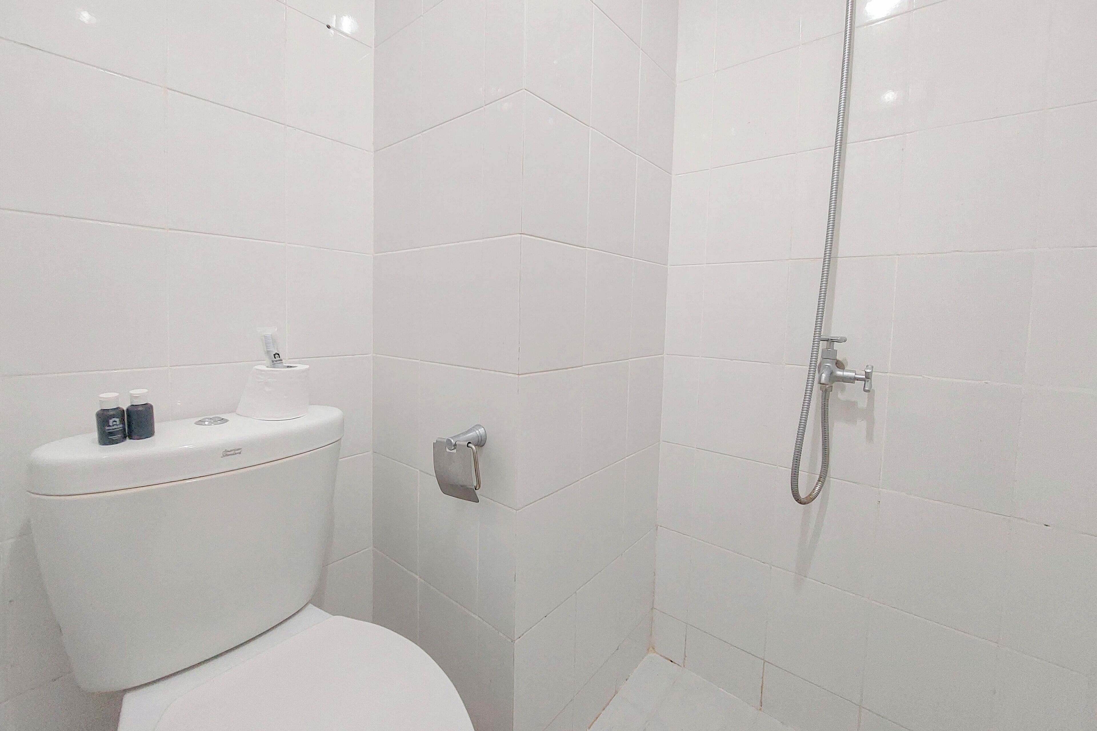 A bathroom with a toilet, a hand dryer, and a shower with a hose.