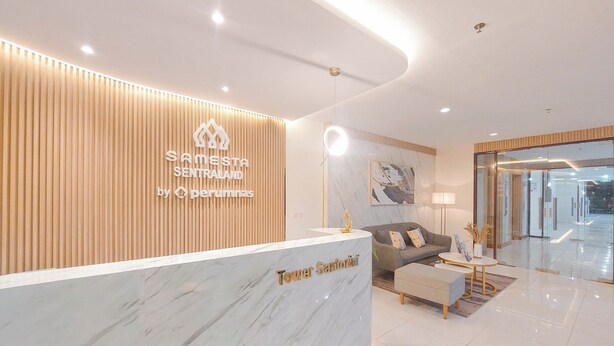 Un área de recepción moderna con un panel de pared de madera, un mostrador de mármol con la leyenda "Tower Santorini" y una zona de estar con sofá y mesa de centro.