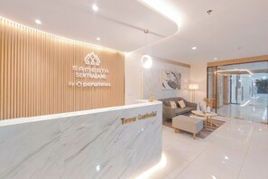 Un espace d’accueil moderne avec un mur revêtu de panneaux en bois, un comptoir de réception en marbre portant l’inscription « Tower Santorini », et un coin salon avec un canapé et une table basse.
