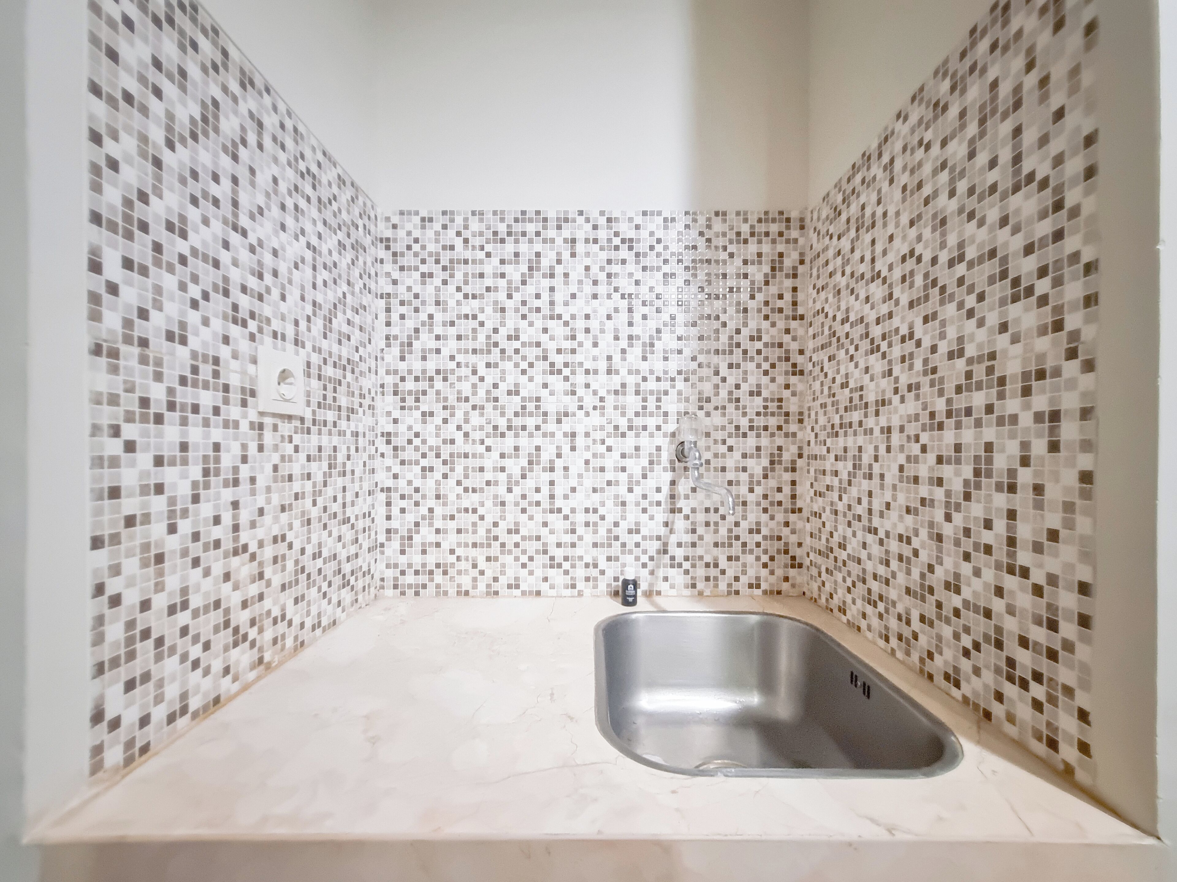 A bathroom with a tiled mosaic wall, a sink, and a faucet.