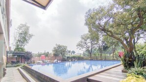 An outdoor swimming pool with a tiled deck, surrounded by trees and a brick wall. - Scenic 2Br At The Edge Bandung Apartment (Cimahi)
