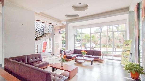 A spacious lobby with a modern sofa set, a staircase, and large windows offering a view of the outdoors. - Scenic 2Br At The Edge Bandung Apartment (Cimahi)