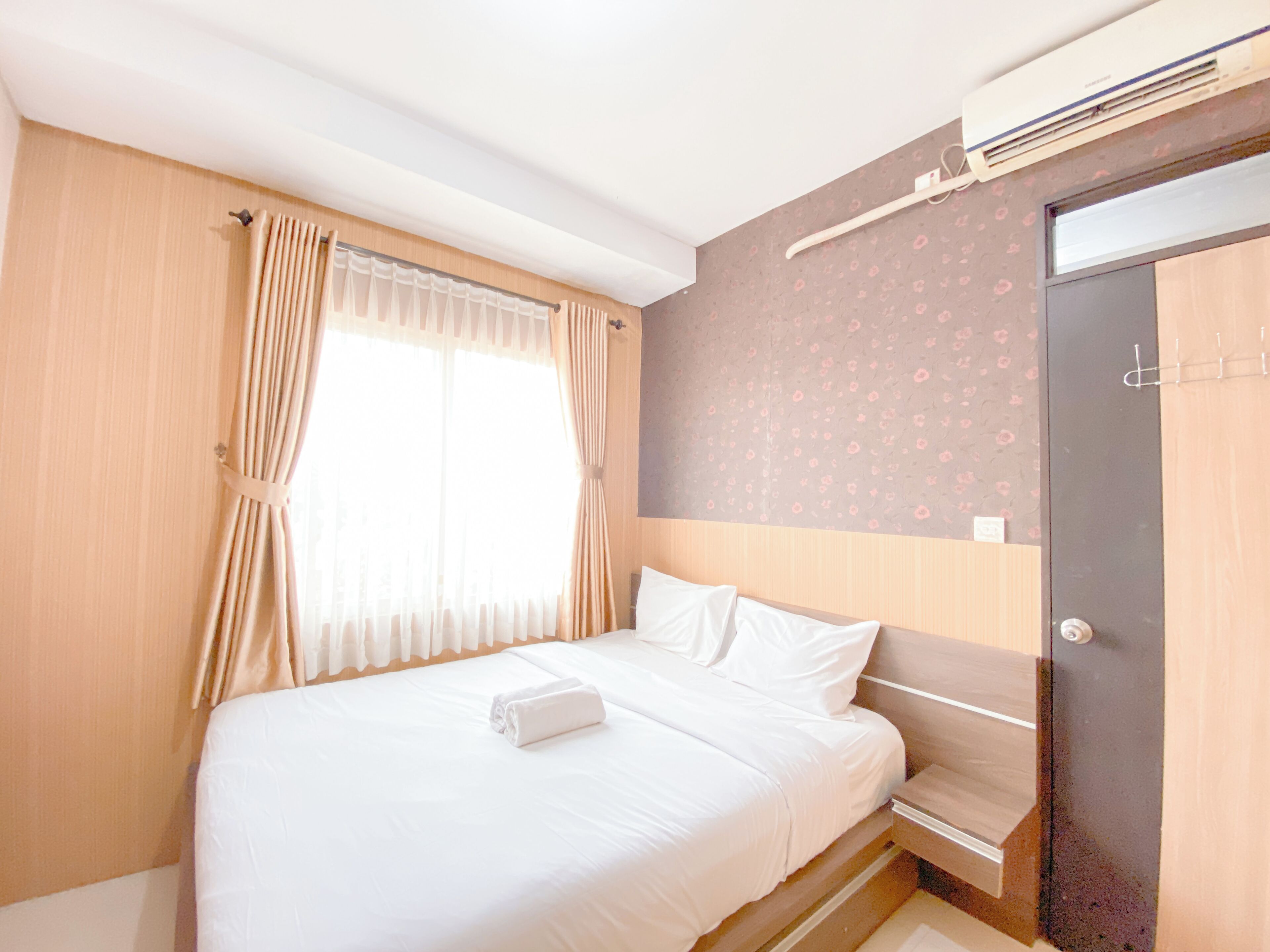 A hotel room with a bed, curtains, an air conditioning unit, and a door.