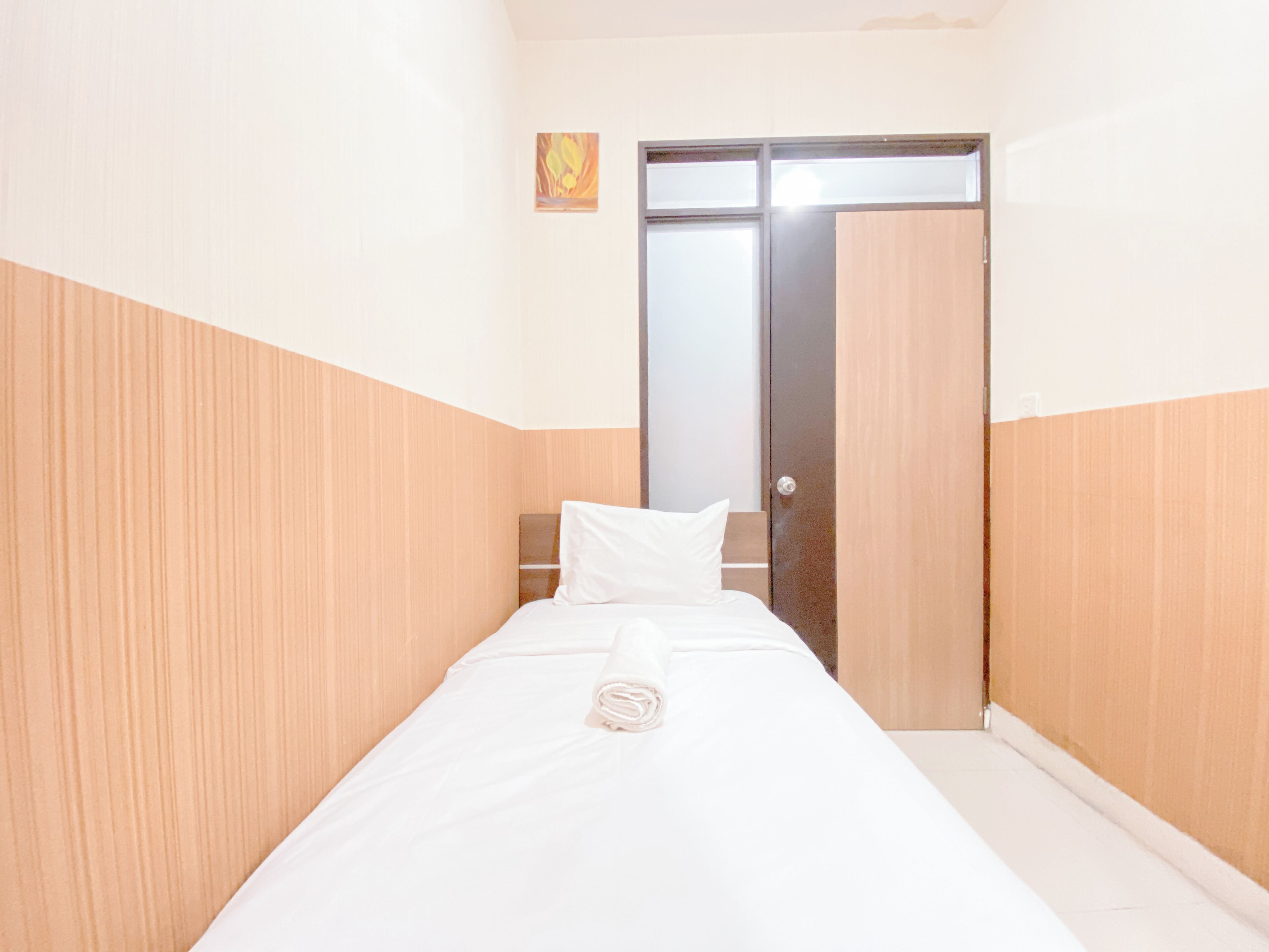 A narrow hotel room with a bed, a wooden wardrobe, and a door with a frosted glass panel.