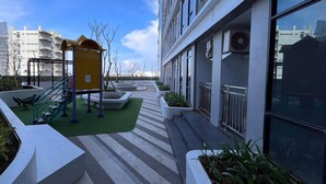 Un espace extérieur moderne comprenant une aire de jeux pour enfants, des zones aménagées pour s’asseoir et des jardinières.