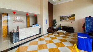 A hotel reception area with a check-in counter, a seating area with a couch and chairs, and a large painting on the wall.