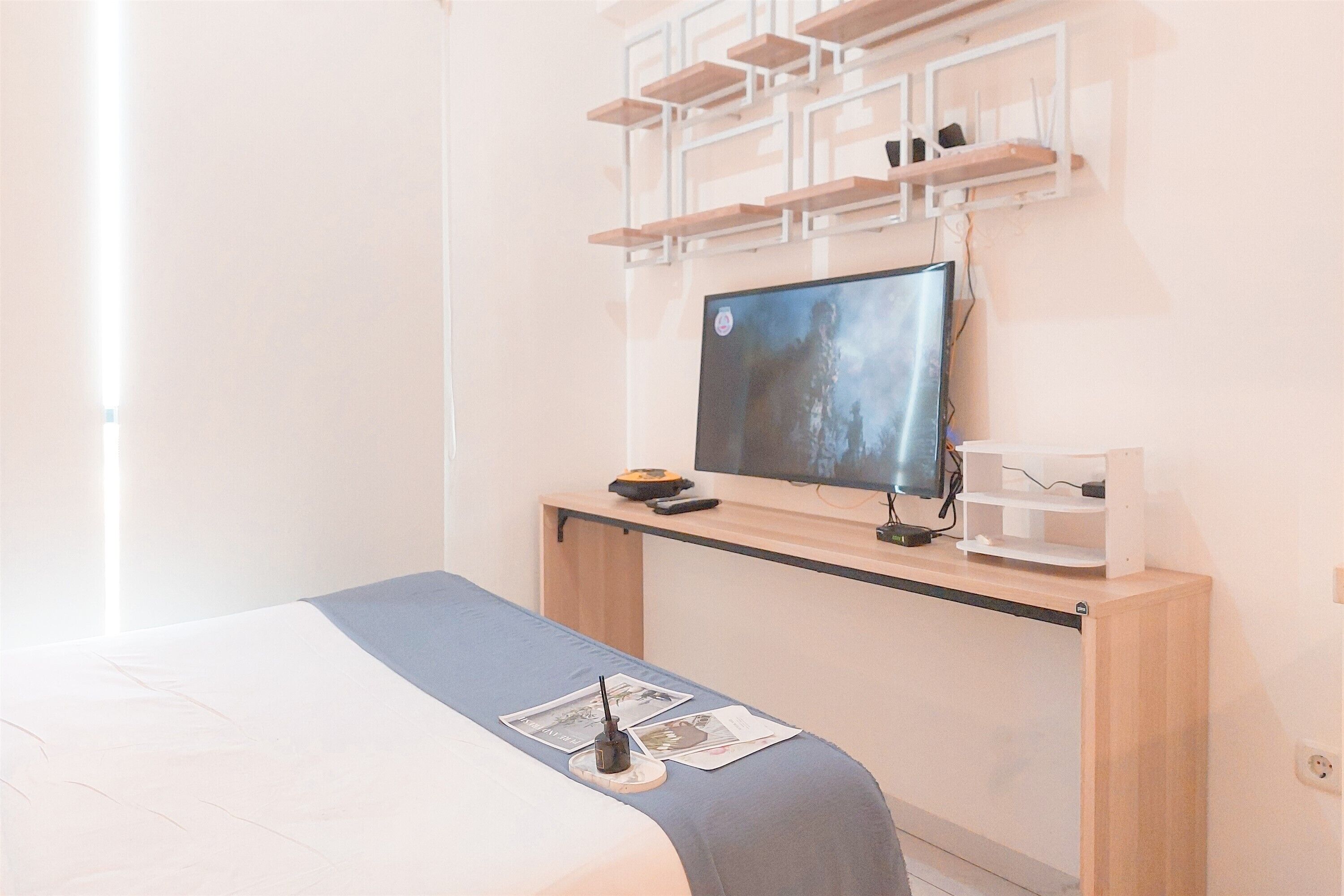 Un dormitorio moderno con cama, escritorio con computadora y televisor de pared.