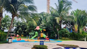 A playground with slides and swings surrounded by palm trees and a water feature.