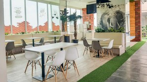 Un espace de restauration intérieur moderne, doté de tables et de chaises, de grandes fenêtres et d’une fresque représentant un éléphant.