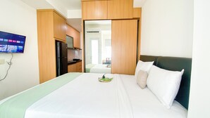 Ein Hotelzimmer mit einem Bett, einem an der Wand befestigten Fernseher und einer Küchenzeile.