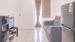 A living room with a flat-screen TV, a sofa, a refrigerator, and a door leading to another room.