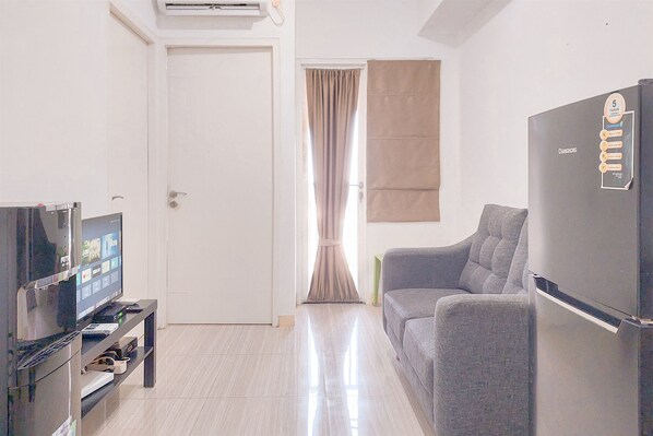 A living room with a flat-screen TV, a sofa, a refrigerator, and a door leading to another room.