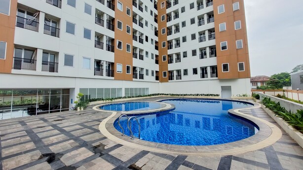 A modern apartment building with a central swimming pool, balconies, and a glass entrance.