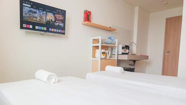 Habitación de hotel con dos camas, un televisor en la pared mostrando opciones de películas, un microondas y una cafetera sobre una repisa.