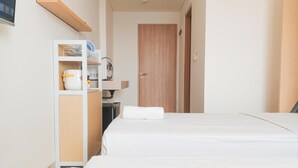 Habitación de hotel con dos camas, un armario de madera, una kitchenette pequeña y una puerta que da a otra habitación.