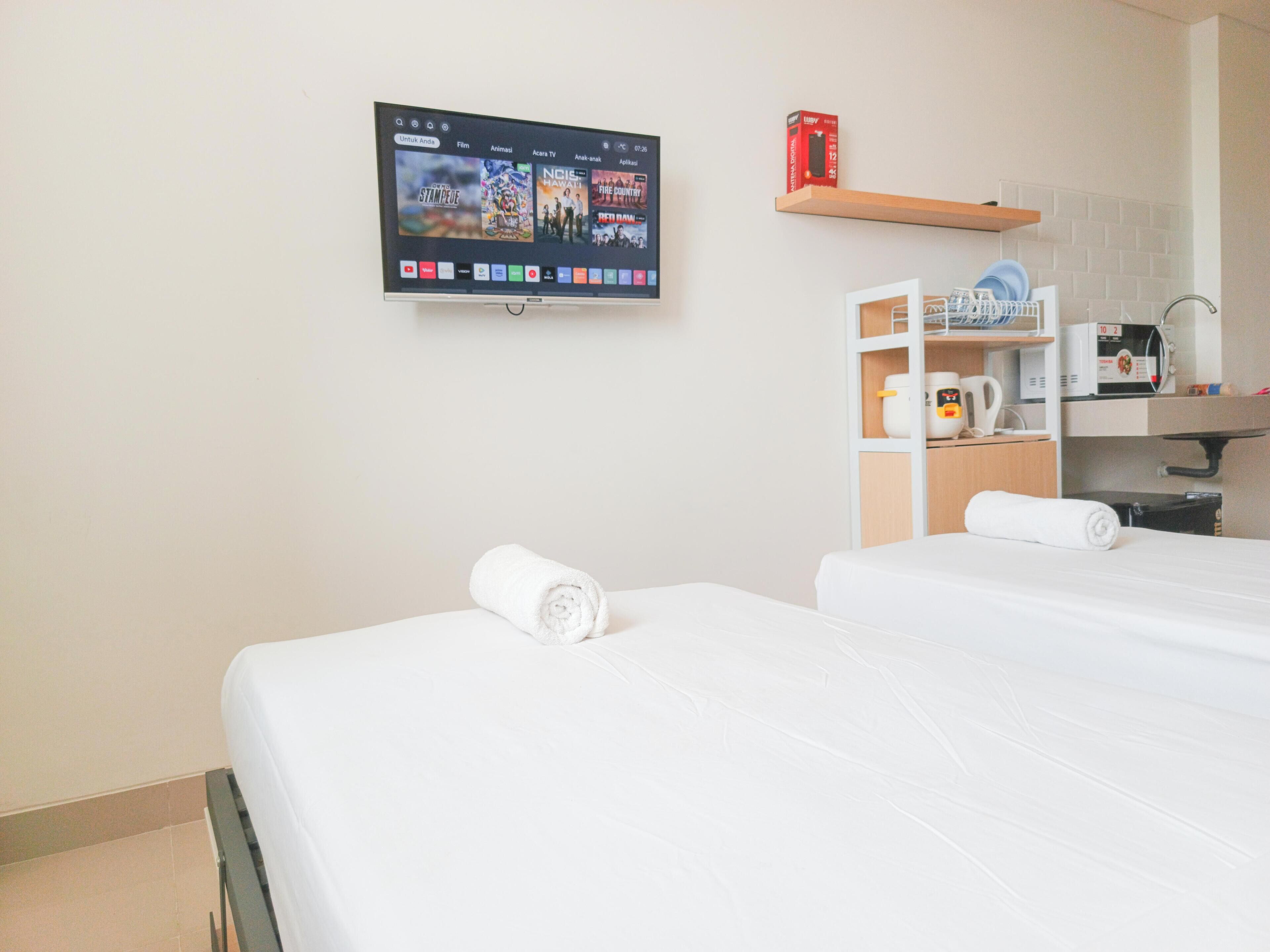 Une chambre d’hôtel avec deux lits, un téléviseur fixé au mur, un four à micro-ondes, une machine à café et une étagère avec une boîte et de la vaisselle.