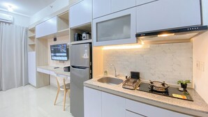 Una cocina moderna con armarios blancos, horno empotrado, refrigerador de acero inoxidable, televisor de pantalla plana y estufa a gas.