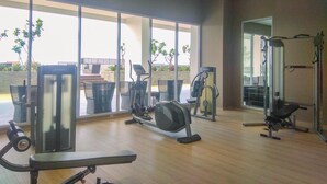 Un gimnasio moderno con diversos equipos de ejercicio, amplias ventanas y vistas a plantas al aire libre.