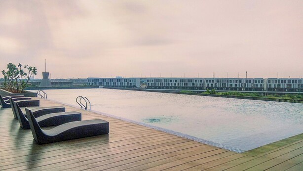 Piscina infinita en la azotea con sillones de descanso y vista a un edificio moderno al otro lado del agua.