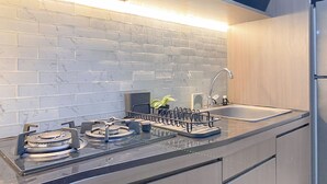 A modern kitchen with white marble tiles, stainless steel appliances, and wooden cabinets. - Cozy Living Studio At Vasanta Apartment (Cikarang)