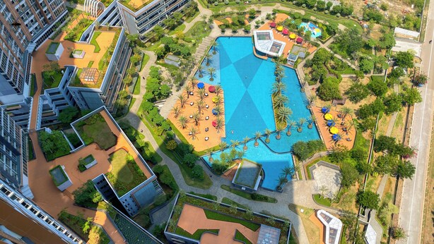 Ein Luftbild eines modernen Hotels mit einem zentralen Schwimmbecken, umgeben von üppiger Vegetation und Außenbereichen mit Sitzgelegenheiten.
