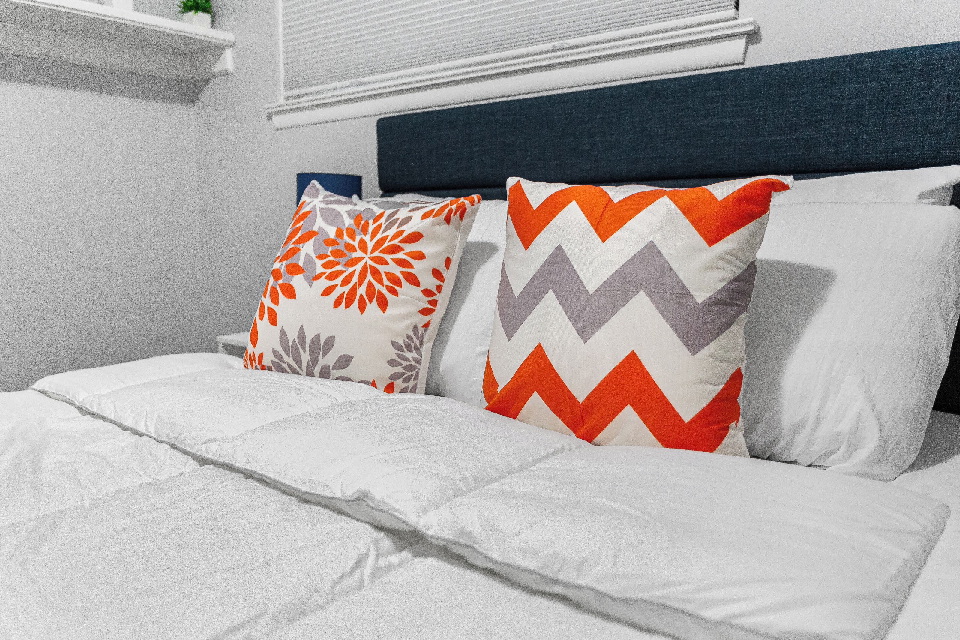 Un lit bien fait, avec une literie blanche et des coussins décoratifs ornés de motifs géométriques.