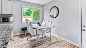 Une cuisine moderne avec des meubles blancs, un plan de travail en granit et un coin repas comprenant une table et des chaises blanches.