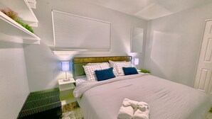 Une chambre à coucher bien rangée, avec un lit, des lampes de chevet, une table de nuit et une fenêtre avec des stores.