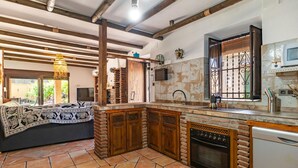 Una cucina con pavimento piastrellato, mobili in legno, forno integrato e una finestra con inferriate decorative.
