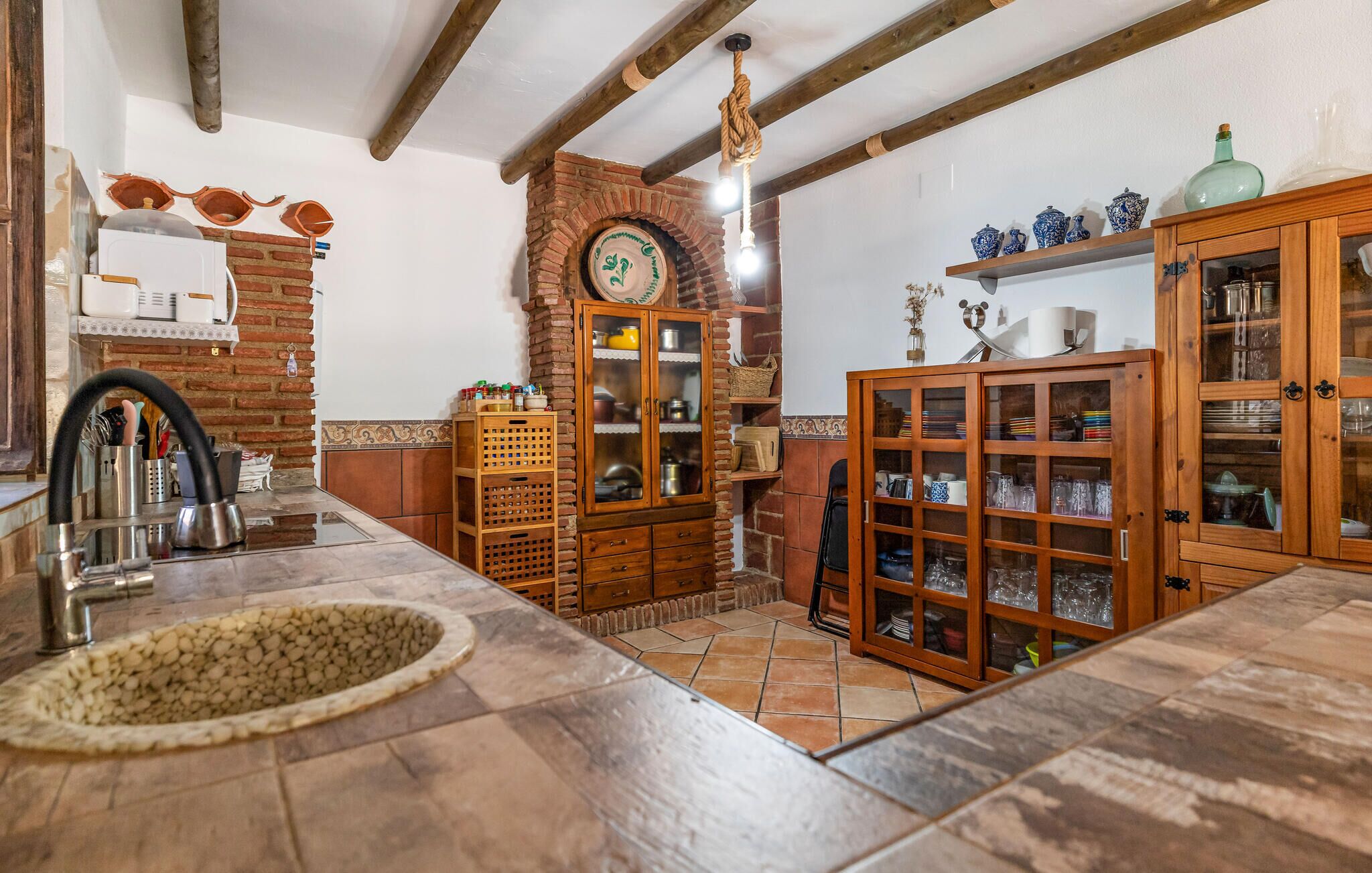 A kitchen with a stone sink, wooden cabinets, and a brick wall.