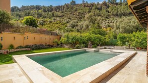 Una piscina rettangolare con bordatura in pietra, immersa in un giardino curato con diverse piante e una statua.