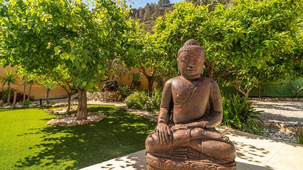 Una statua del Buddha seduto in un giardino con alberi e un vialetto in pietra.
