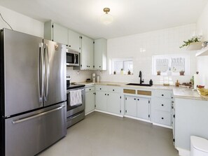 A modern kitchen with stainless steel appliances, white cabinetry, and a large window providing natural light.