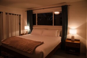 A single bed with a headboard, two bedside lamps, a nightstand, and a window with curtains.