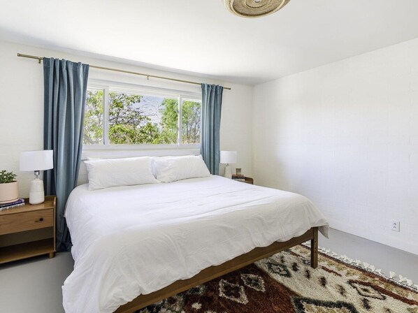 A bedroom with a bed, two bedside tables, a window with curtains, and a rug.