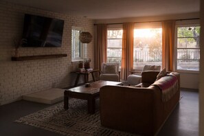 A living room with a brick wall, a flat-screen TV, a sofa, a coffee table, and a window with curtains.