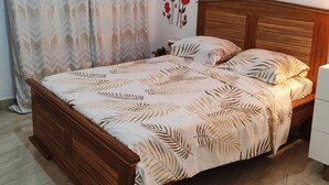 Een slaapkamer met een houten bed, een bed met een geborduurd sprei, een nachtkastje en een wanddecoratie van rode bloemen.