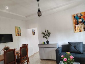 A living room with a TV, a dining table with chairs, a sofa, and a potted plant.