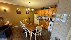 Un comedor con mesa y sillas de madera, una araña y una cocina con armarios de madera y electrodomésticos blancos.